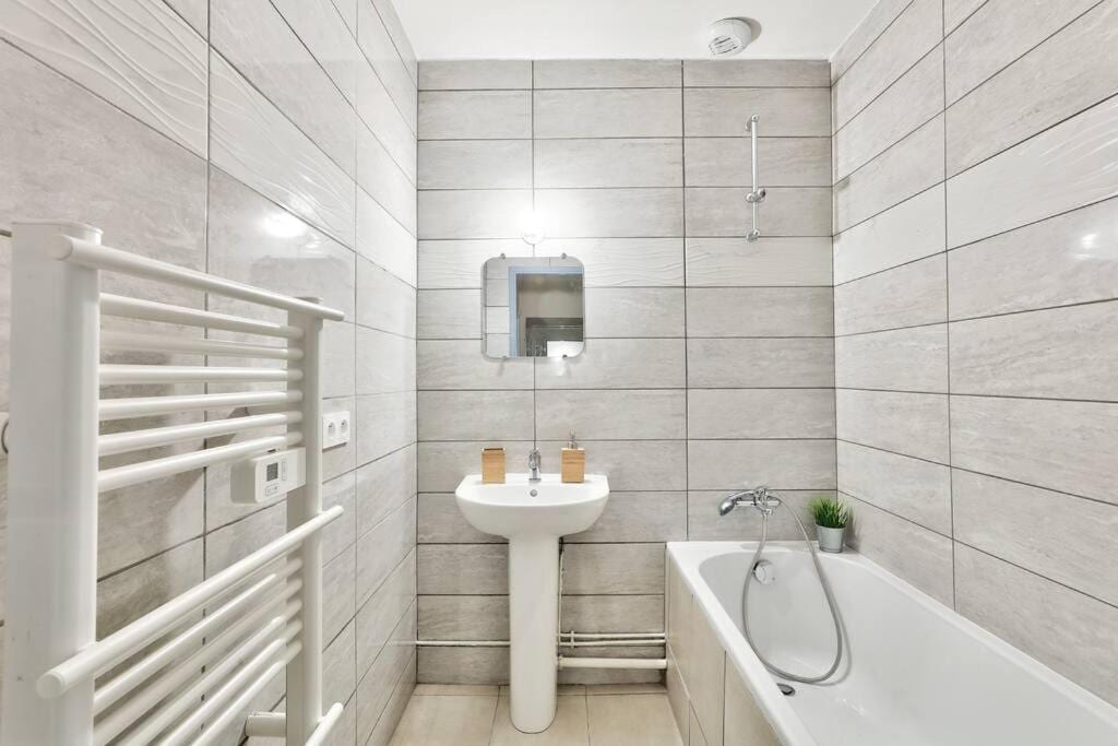 Salle de bain — Carrelage gris, baignoire blanche, lavabo suspendu, miroir, radiateur blanc